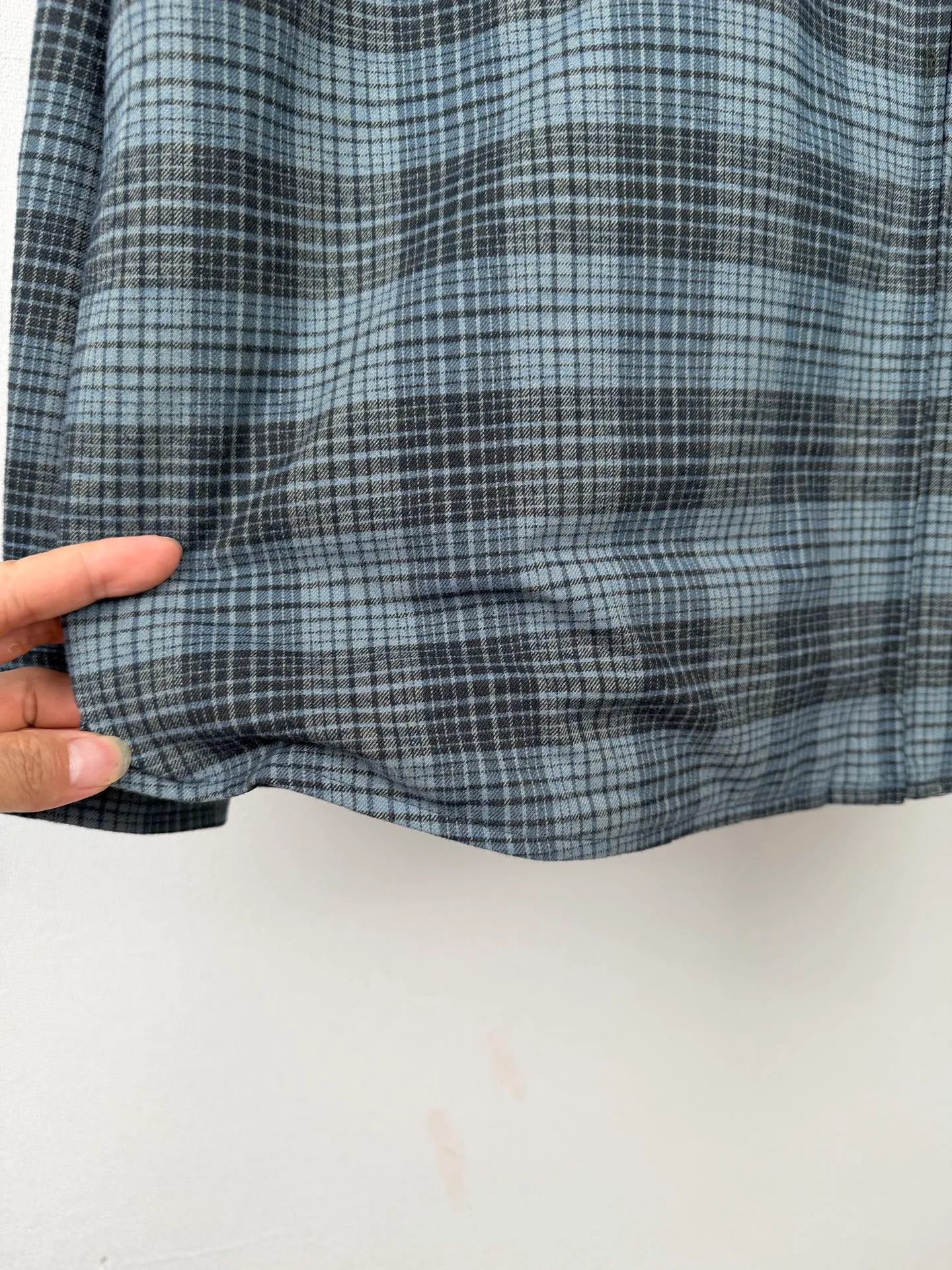 BALENCIAGA/balenciaga blue and gray plaid zipper pocket logo quilted jacket combines a three-layer structure of plaid woven fabric, filling cotton, and lining, and integrates plaid alignment technology and quilted garment production standards. There are multiple process difficulties in the whole process. The surface layer of the body is made of blue-gray Retro plaid fabric, and the cutting machine production strictly follows the global grid standards. The arrangement direction of the cutting pieces is fixed and cannot be changed at will. The horizontal and vertical lines of shoulder seams, side seams, and zipper placket joints must be consistent and coherent. The left chest patch pocket is cut independently, and the bag check pattern must be aligned with the front reference pattern. Slight deviations will destroy the visual integrity and directly increase fabric loss and cutting time. The most difficult part of the style is the three-layer composite sewing. The outer plaid fabric, filling cotton, and lining fabric have different physical properties, and the preshrinking processing parameters need to be adjusted separately. Pressure and temperature control are crucial during lamination operations. Once the parameters are out of balance, it can easily cause fabric stretch and distortion, plaid dislocation, and wrinkles and bulges in garments. At the same time, it is necessary to reasonably plan the quilting line to avoid the visual beauty of the grid pattern from being cut by the lines on the basis of firmly fixing the cotton layer and preventing cotton from running away. The placket adopts a centered zipper structure. It is difficult to sew the zipper tape and the quilted panels. It is required that the width of the left and right plackets be equal, the zipper routing is straight and smooth, and there is no lag in opening and closing. When the shirt lapel is filled with cotton, the thickness of the cotton needs to be controlled to prevent the collar from becoming bloated and unnaturally folded. The metal nameplate of the chest pocket is sewn at fixed points to avoid pulling the fabric during the operation and ensure that the plaid pattern is smooth and not deformed. The quilted material increases the overall thickness of the fabric. When sewing, you need to continuously adjust the presser foot pressure and stitch length to adapt to changes in sandwich thickness. The low-temperature and gentle ironing process is used for post-finishing to prevent the plaid from fading and the cotton layer from clumping due to high temperatures. From the precise alignment of cutting pieces, three-layer fabric pretreatment, composite quilting to garment finalization inspection, the processes are interlocking and the error tolerance rate is extremely low, testing the accuracy of plate making, equipment control and turning technology. Size:XS S M L